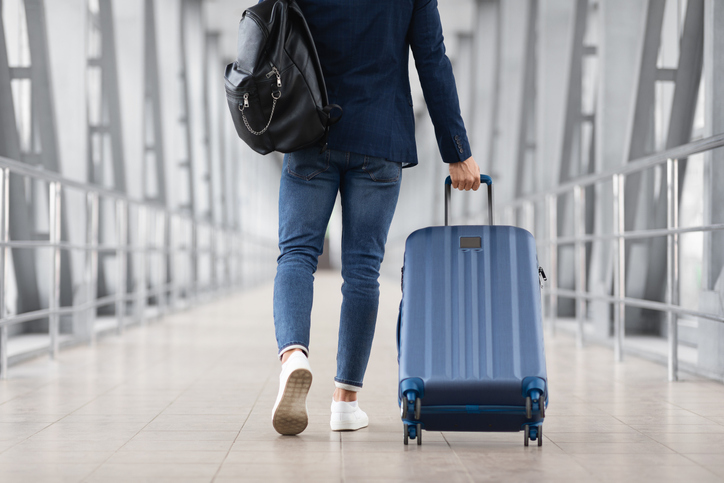 スーツケースとバックパックを持ち空港を歩く男